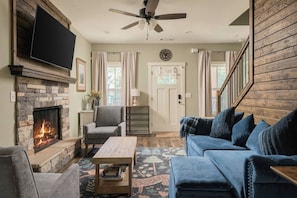 A living room with a stone fireplace, a blue sofa, a wooden coffee table, and a ceiling fan.