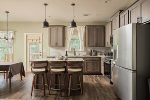 Une cuisine moderne avec des meubles en bois, un réfrigérateur en acier inoxydable et un coin bar avec des tabourets.