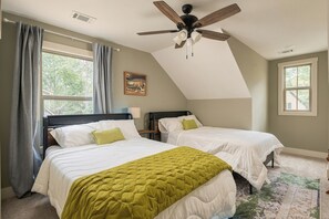 A bedroom with two beds, a ceiling fan, and large windows.