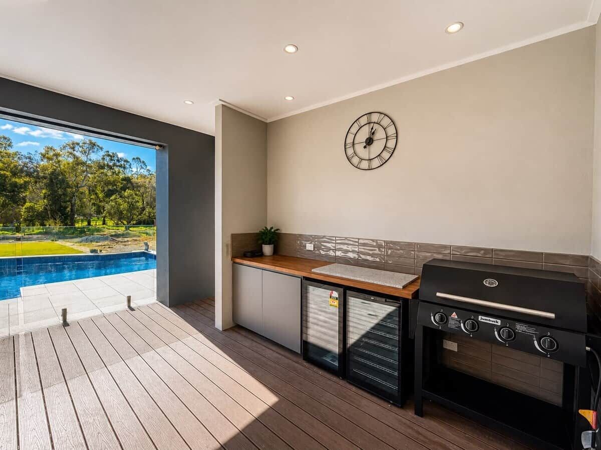 A modern outdoor kitchen with a built-in grill, a small refrigerator, and a clock on the wall.