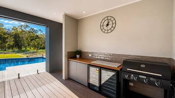 A modern outdoor kitchen with a built-in grill, a small refrigerator, and a clock on the wall.