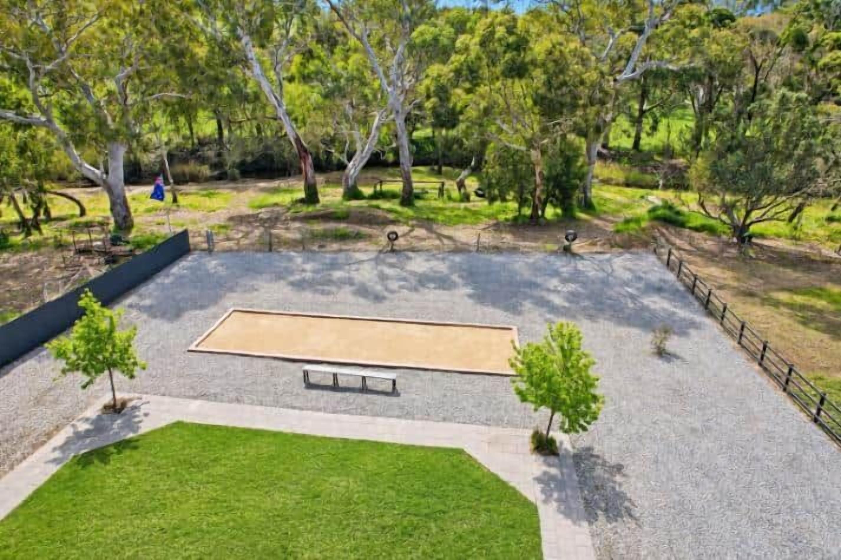 A park with a rectangular sandy play area, a bench, and a paved walkway.