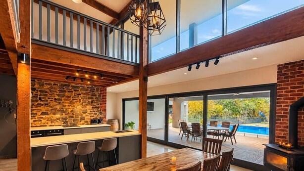 A spacious kitchen with a stone backsplash, a dining area with a wooden table and chairs, and a view of a swimming pool. - Blumberg Mews - Stunning Adelaide Hills Retreat Near Barossa (Birdwood)