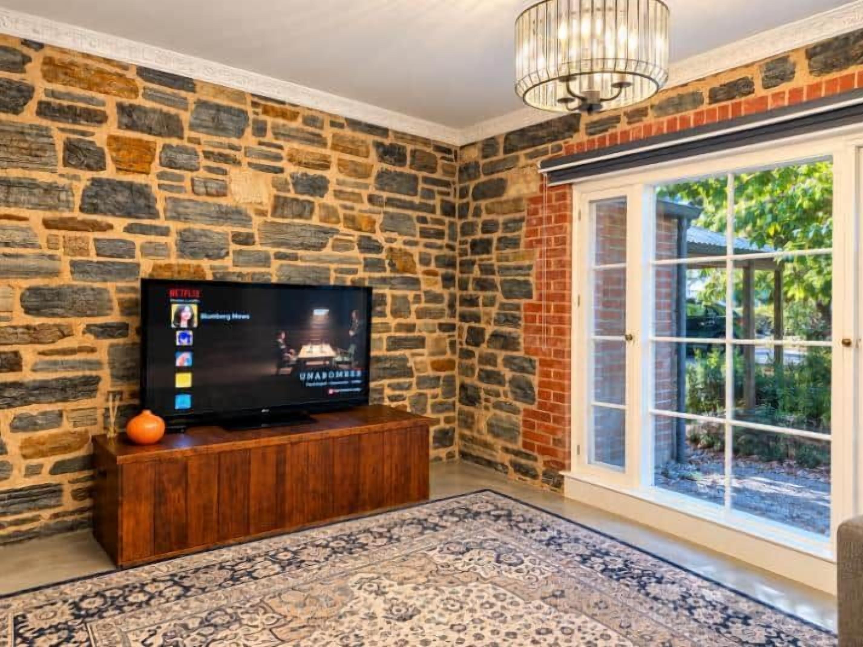 Une pièce avec un mur en pierre, un meuble de rangement en bois, un téléviseur et un tapis à motifs.