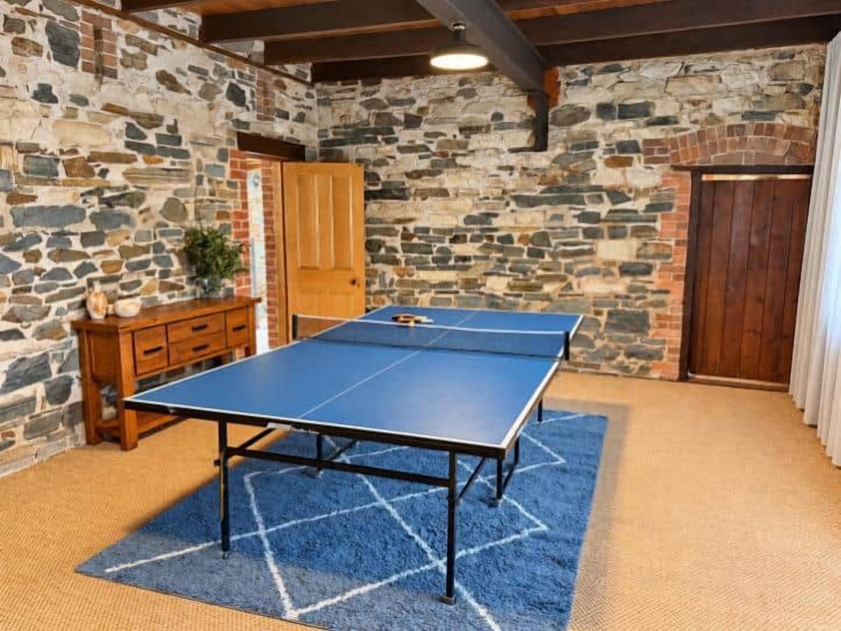 A ping pong table in a room with stone walls and a wooden cabinet.
