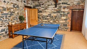 A ping pong table in a room with stone walls and a wooden cabinet.