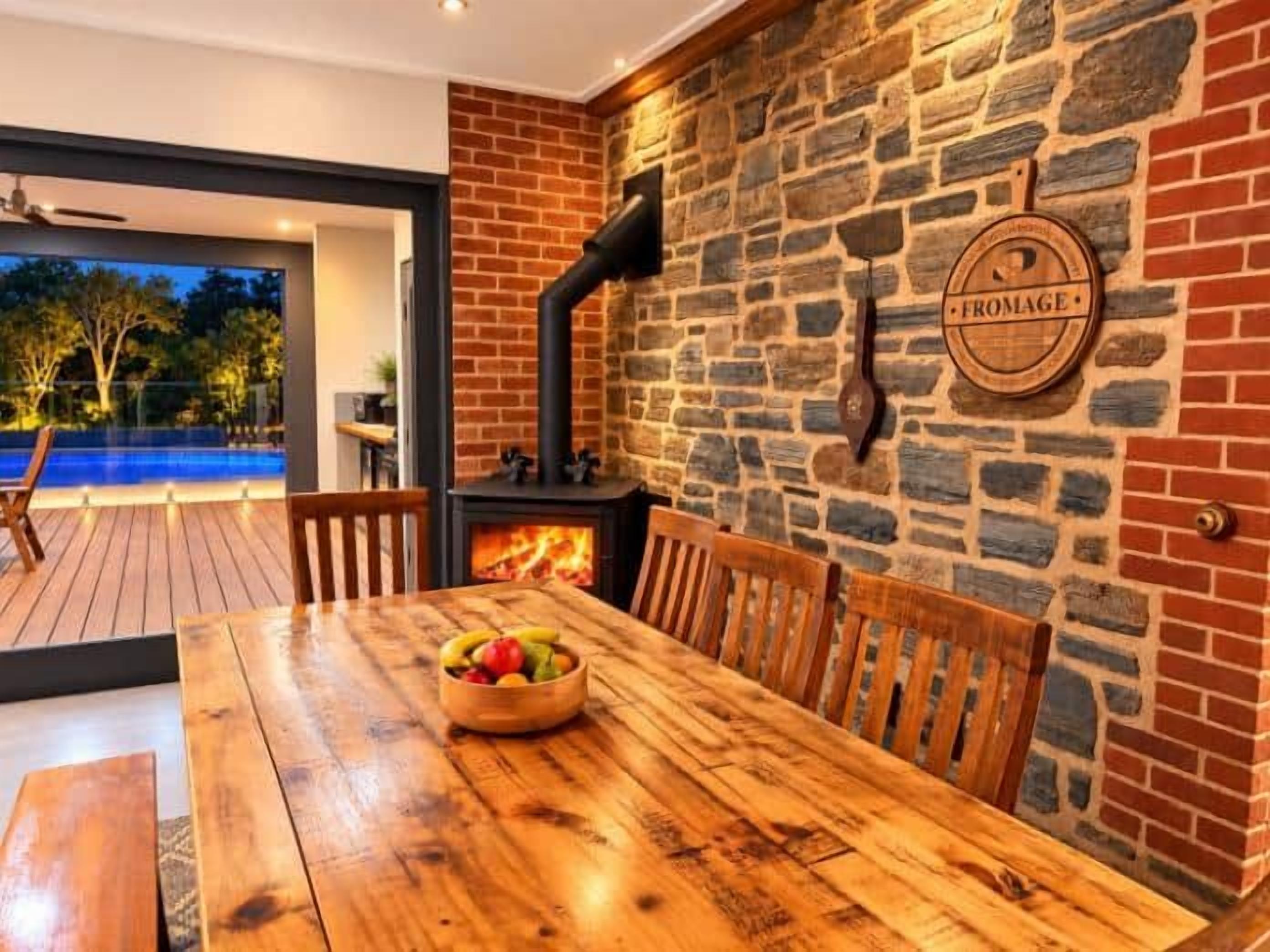 A wooden dining table with chairs, a bowl of fruit, and a stone wall with a fireplace.