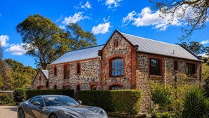 A stone building with a gravel driveway and a parked sports car. - Blumberg Mews - Stunning Adelaide Hills Retreat Near Barossa (Birdwood)
