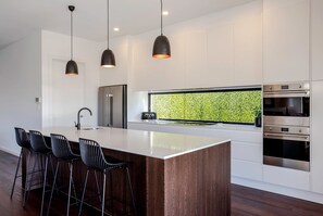 Cozinha moderna com ilha central, banquetas, iluminação pendente e eletrodomésticos embutidos.