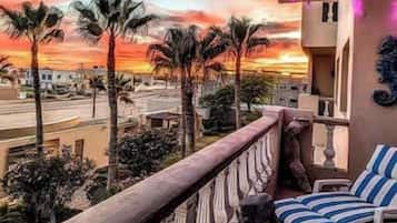Un balcon offrant une vue sur un coucher de soleil, des palmiers et des chaises longues à rayures.