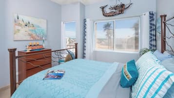 Quarto com cama, mesa de cabeceira, janela com cortinas, pintura na parede e objeto decorativo sobre a cama.