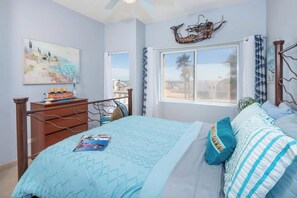 A bedroom with a bed, a nightstand, a window with curtains, a painting on the wall, and a decorative piece above the bed.