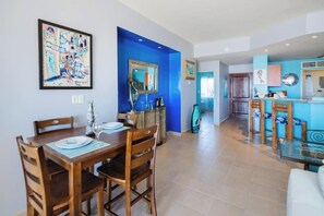 Un coin repas avec une table et des chaises en bois, une cuisine aux touches de bleu et un salon avec un canapé.