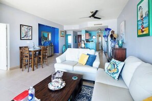 A modern living room with a white sofa, a wooden coffee table, and a dining area with wooden chairs. - Corona Del Mar 205 |2BR| Ocean View | Las Conchas (Las Conchas)