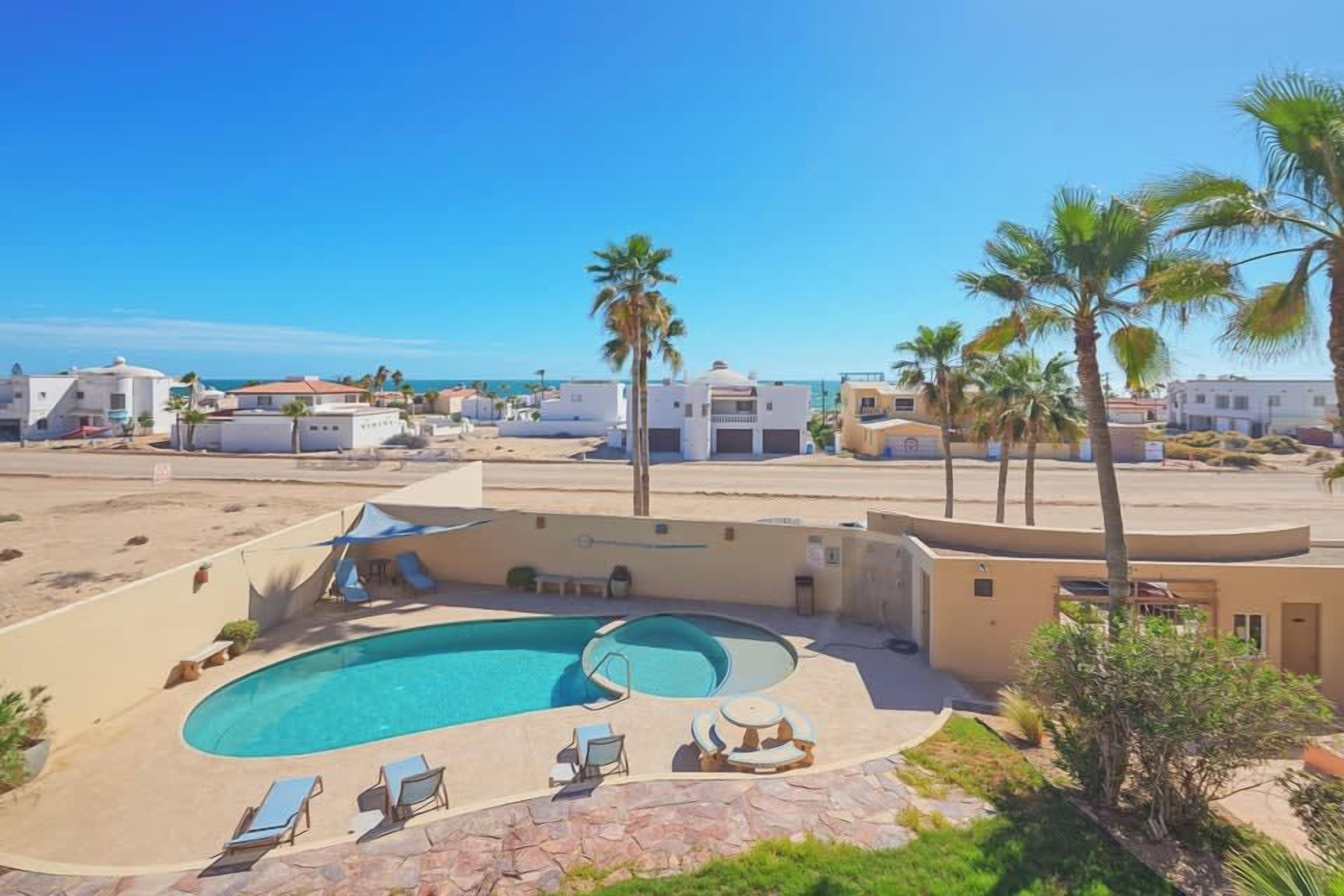 Une piscine avec des chaises longues, un espace de détente abrité et une vue sur la plage et l’océan.