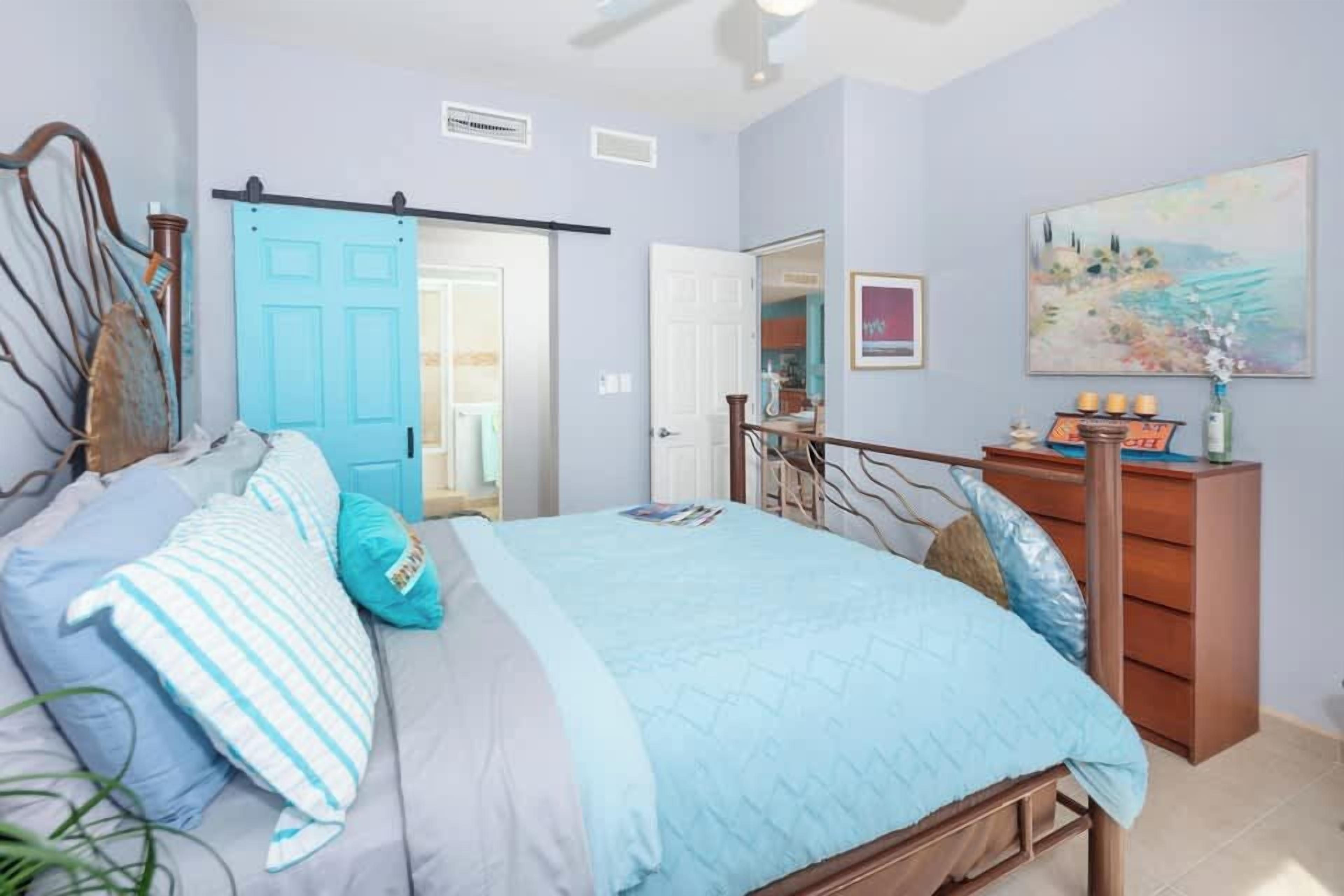 Une chambre à coucher avec un lit, une commode, une porte et un tableau accroché au mur.
