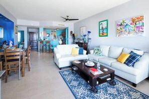 A modern living room with a white sofa, wooden dining table, and blue patterned rug. - Corona Del Mar 205 |2BR| Ocean View | Las Conchas (Las Conchas)