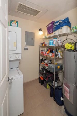 A laundry room with a washing machine, shelves with cleaning supplies, and a water heater.