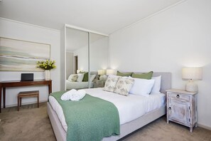 A hotel room with a bed, bedside table, lamp, and a desk with a laptop. - St Kilda Ocean View with Parking (Saint Kilda West)