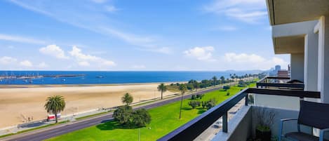 Un balcon donnant sur une plage, une route et un paysage urbain lointain.