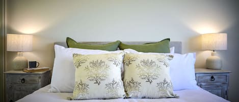 Un lit bien fait, avec une literie blanche et deux coussins décoratifs ornés d’un motif inspiré de la nature.