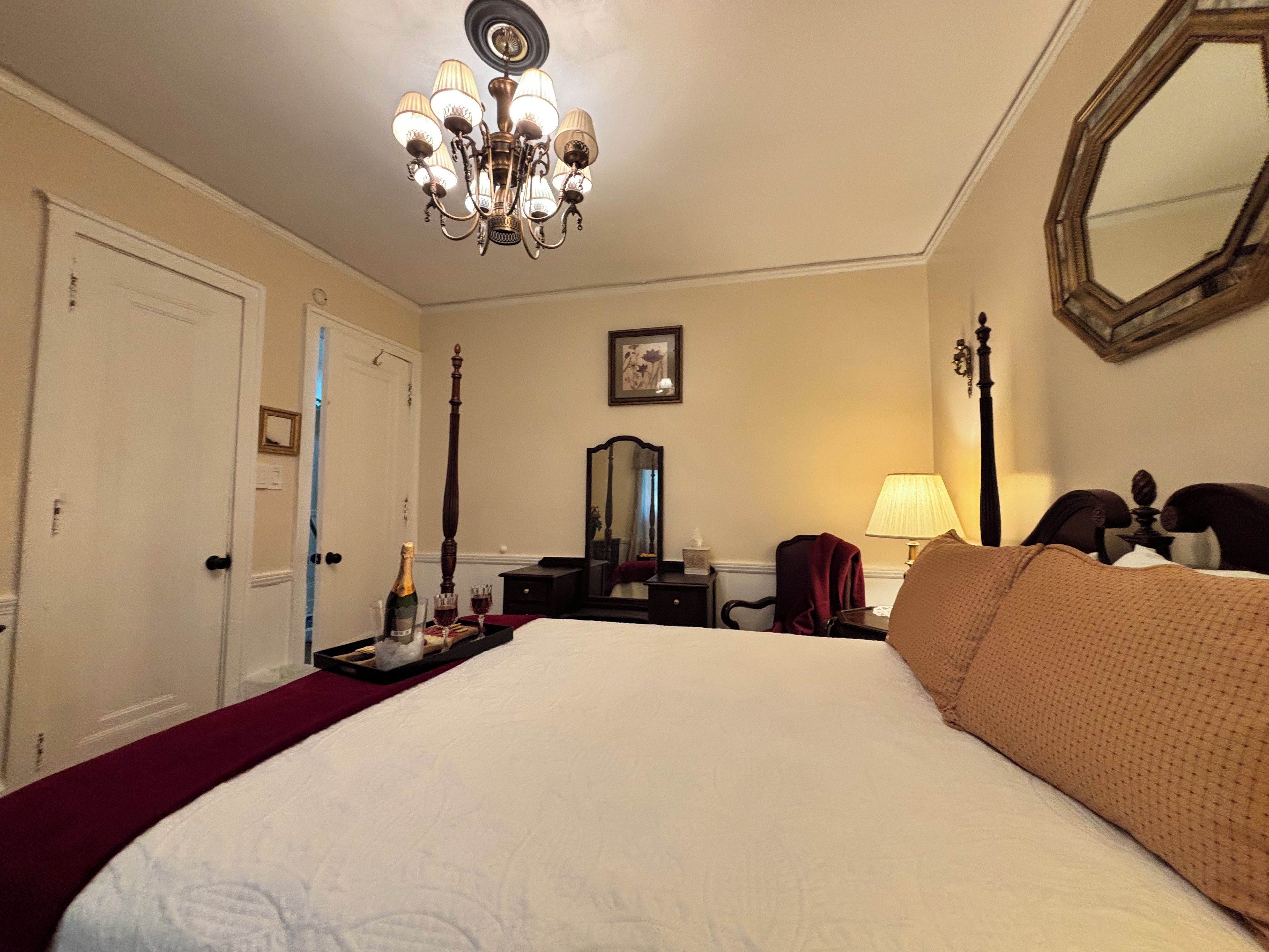 A hotel room with a large bed, a chandelier, a mirror, a bedside table, and a door.