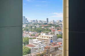 Un paisaje urbano con edificios residenciales y comerciales, cielo despejado y vista a través de una ventana que muestra parcialmente el interior de un edificio.