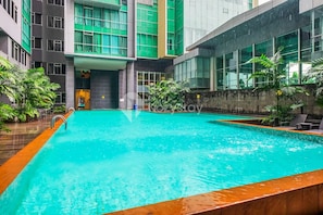 Una piscina interior moderna con agua azul cristalina, rodeada por una terraza de madera y plantas en macetas.