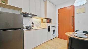 Una cocina compacta con lavadora integrada, microondas y refrigerador de acero inoxidable.
