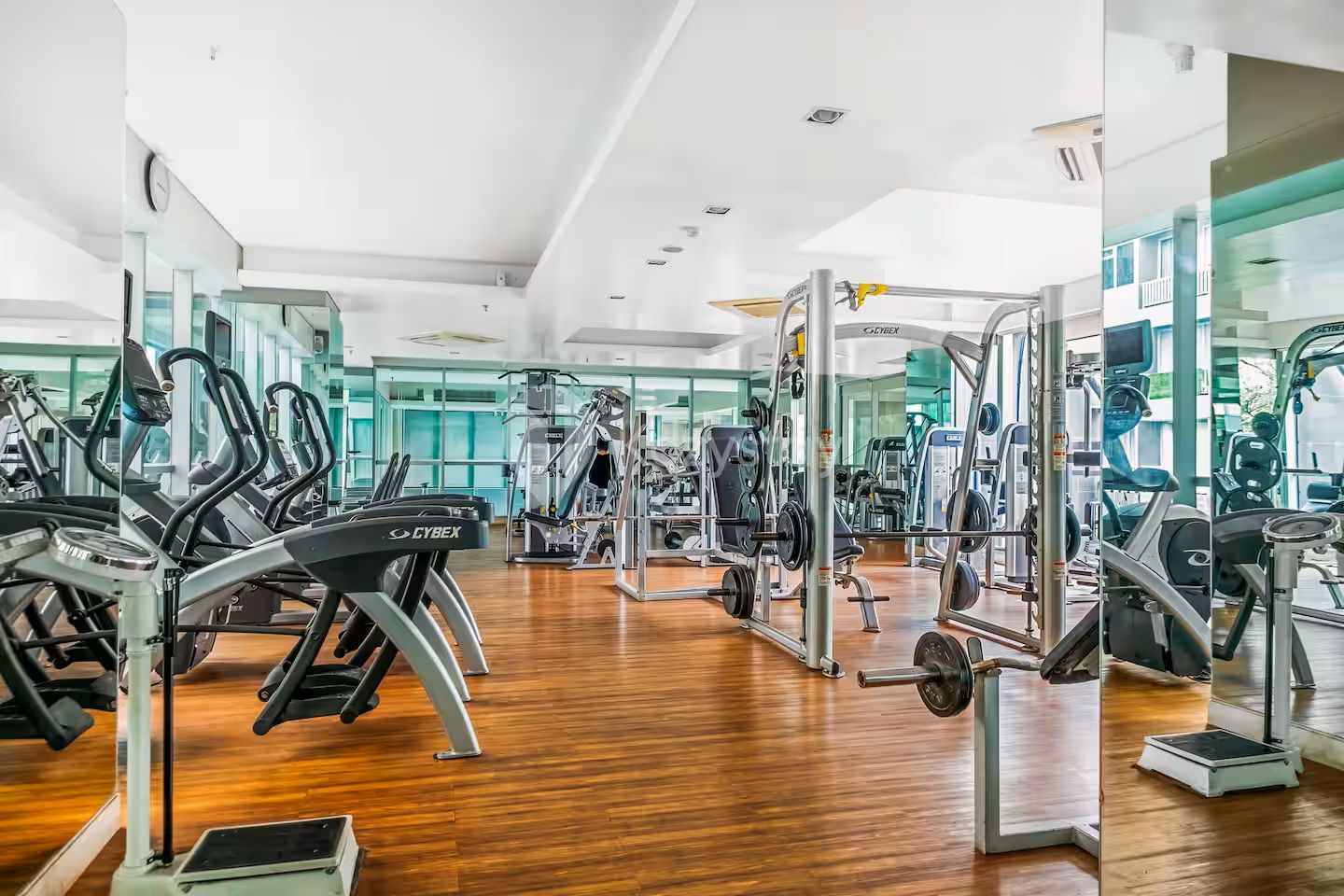 Un gimnasio con máquinas de cardio, equipo de levantamiento de pesas y espejos en las paredes.