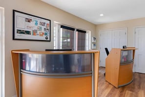 A reception desk with a computer, a framed informational poster, and a door in the background.