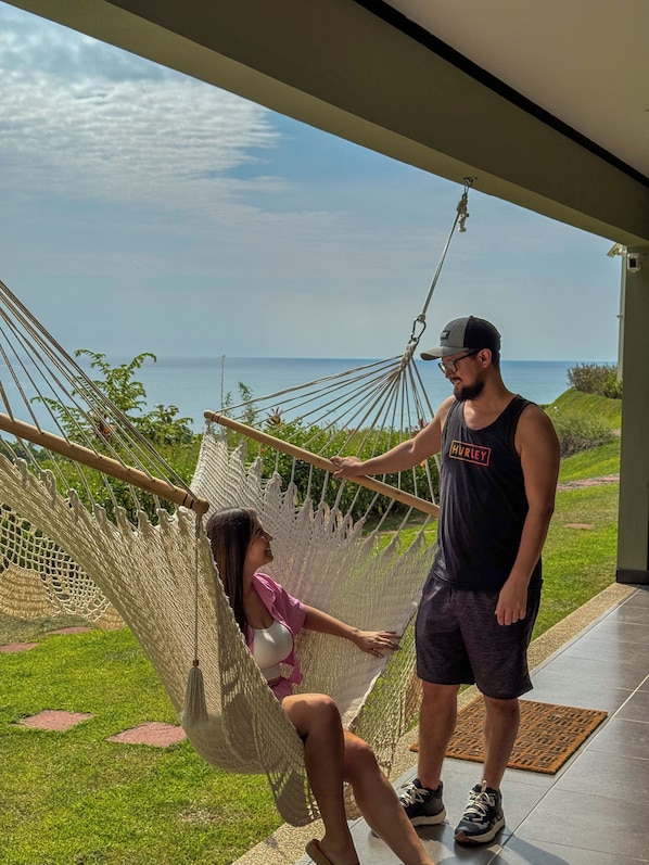A hammock with a view of the ocean, a person standing, and a person sitting.