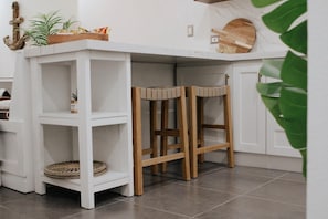 A white kitchen island with built-in wooden stools, a woven basket, and a wooden cutting board on top.
