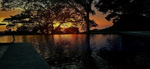Un atardecer sobre un cuerpo de agua con siluetas de árboles contra el cielo.
