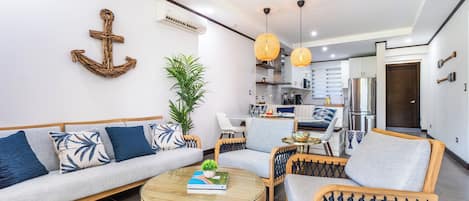 A modern living room with a sofa, chairs, a coffee table, and a kitchen in the background.