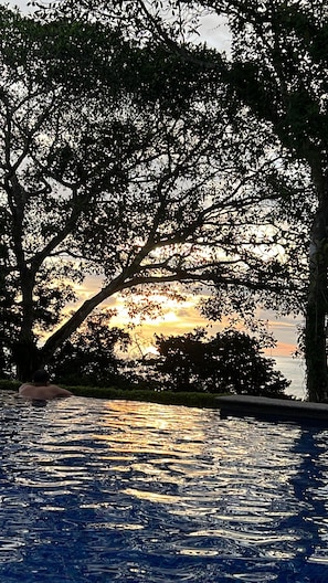 A swimming pool with a sunset view, surrounded by trees.