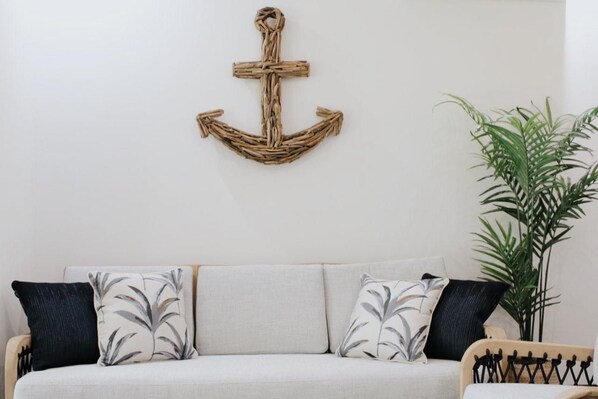 A living room with a sofa, two pillows, a wall-mounted anchor decoration, and a potted plant.