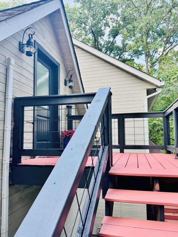 A wooden deck with a metal railing, a window with a view of trees, and a red bench.