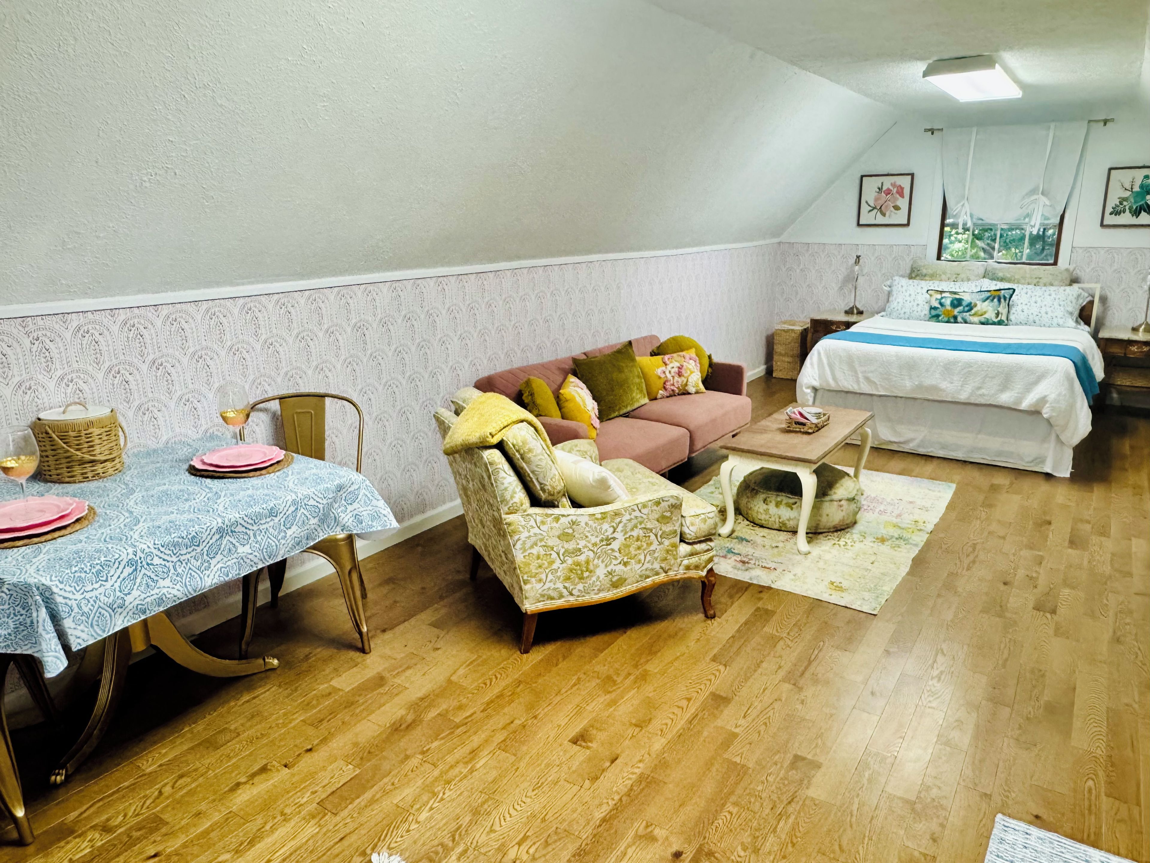 A cozy room with a dining table set for two, a sofa, a chair, and a bed.