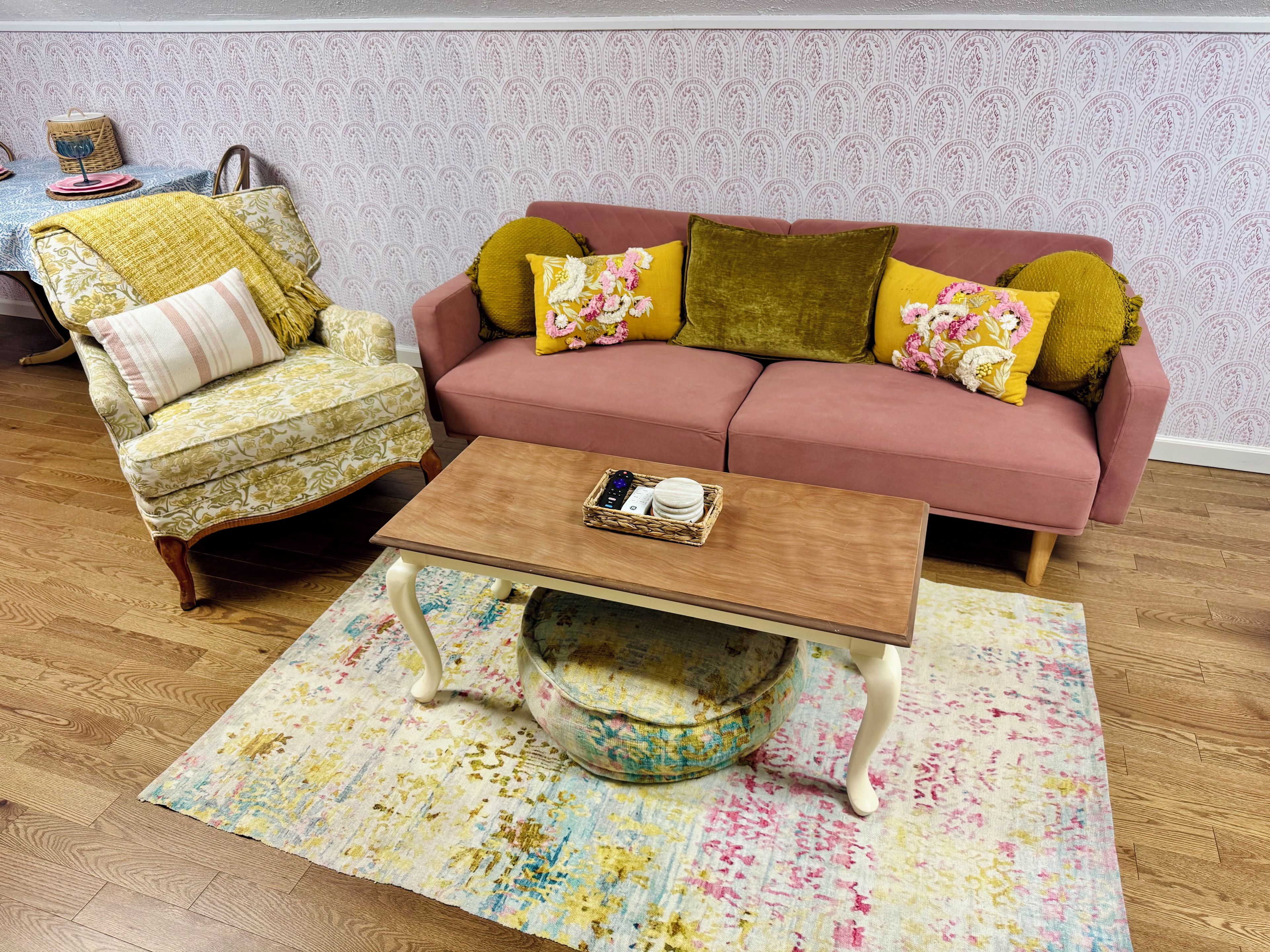 Una sala de estar con sofá, sillón, mesa de centro y alfombra estampada.