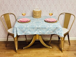A dining table with a patterned tablecloth, two chairs with gold legs, and a wicker basket on the table.