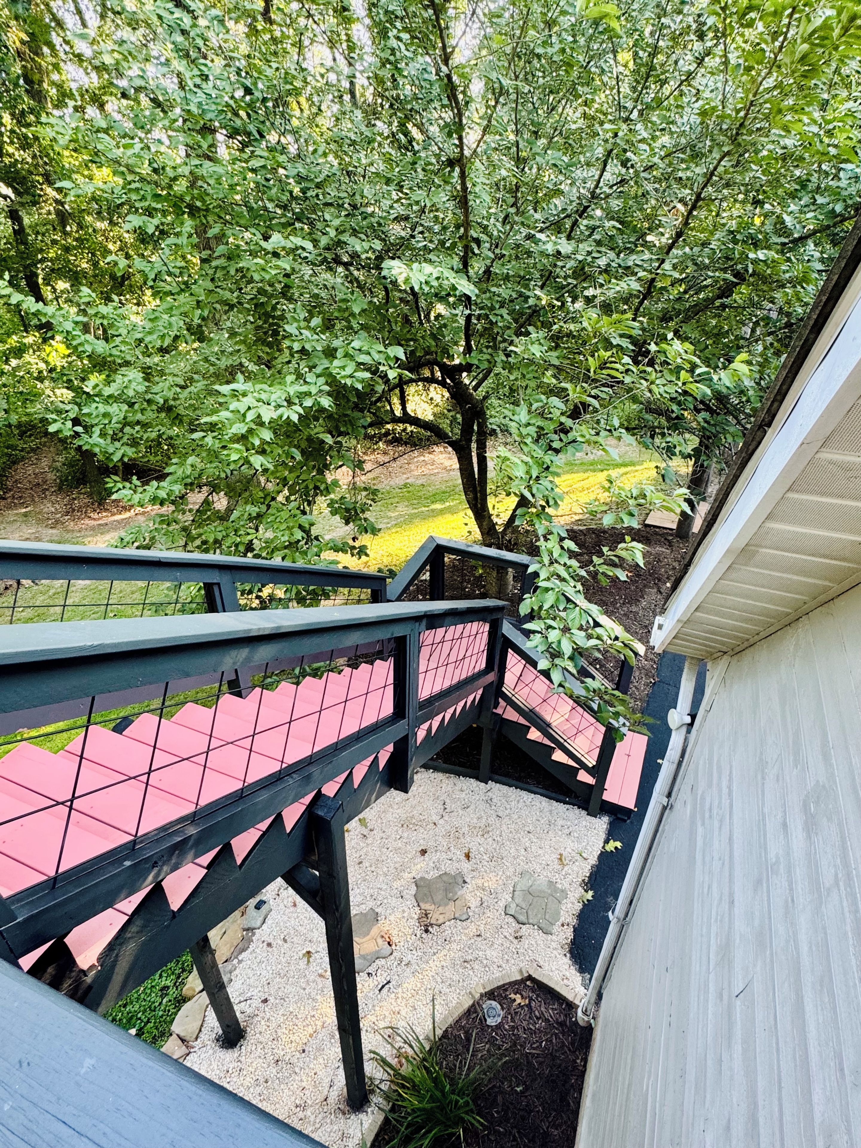 A staircase with a black railing leading to a covered outdoor area with a view of a garden and trees.