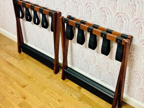 A wooden shoe rack with multiple black straps against a patterned wallpaper background.