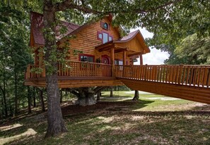 Eine Holzjagdhaus mit einer Terrasse und einer Brücke, umgeben von Bäumen.