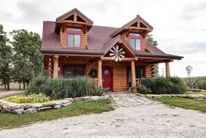 A log cabin with a red door, two chimneys, and a windmill in the background. - Branson | Family Ozarks Retreat | Pool + Fitness (Ridgedale)