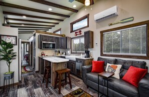 A compact kitchen with a central island, a dining area with a sofa, and a large window with blinds. - Branson | Family Ozarks Retreat | Pool + Fitness (Ridgedale)