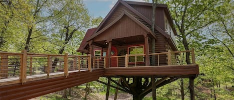 A wooden treehouse with a balcony and a wooden bridge.