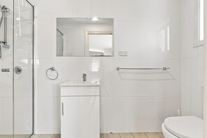 Ein modernes Badezimmer mit Duschkabine aus Glas, Waschbecken mit Spiegel und Toilette.