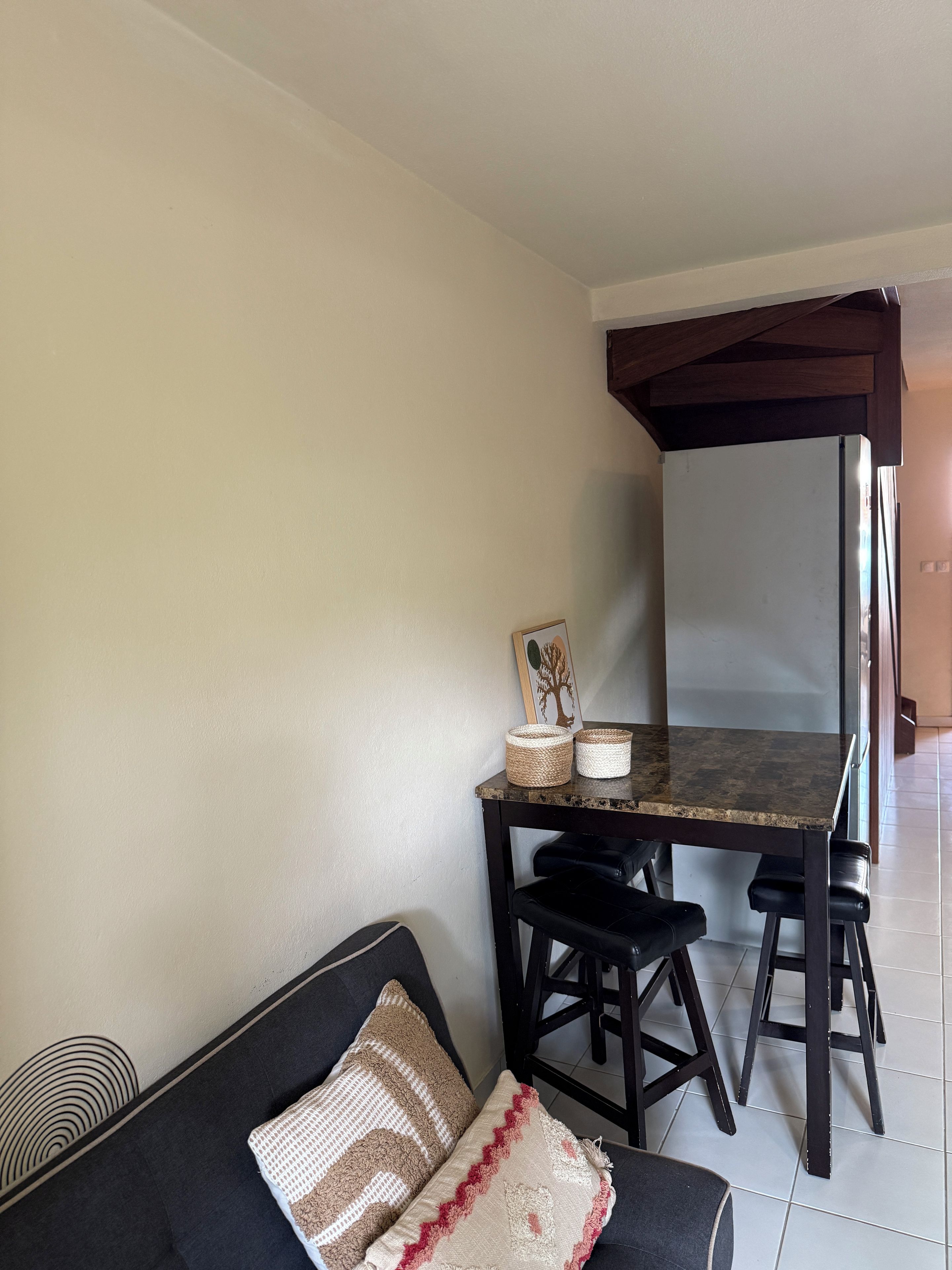 Een kamer met een donkergrijze bank, een eettafel met twee stoelen, en een plafond met houten balken.