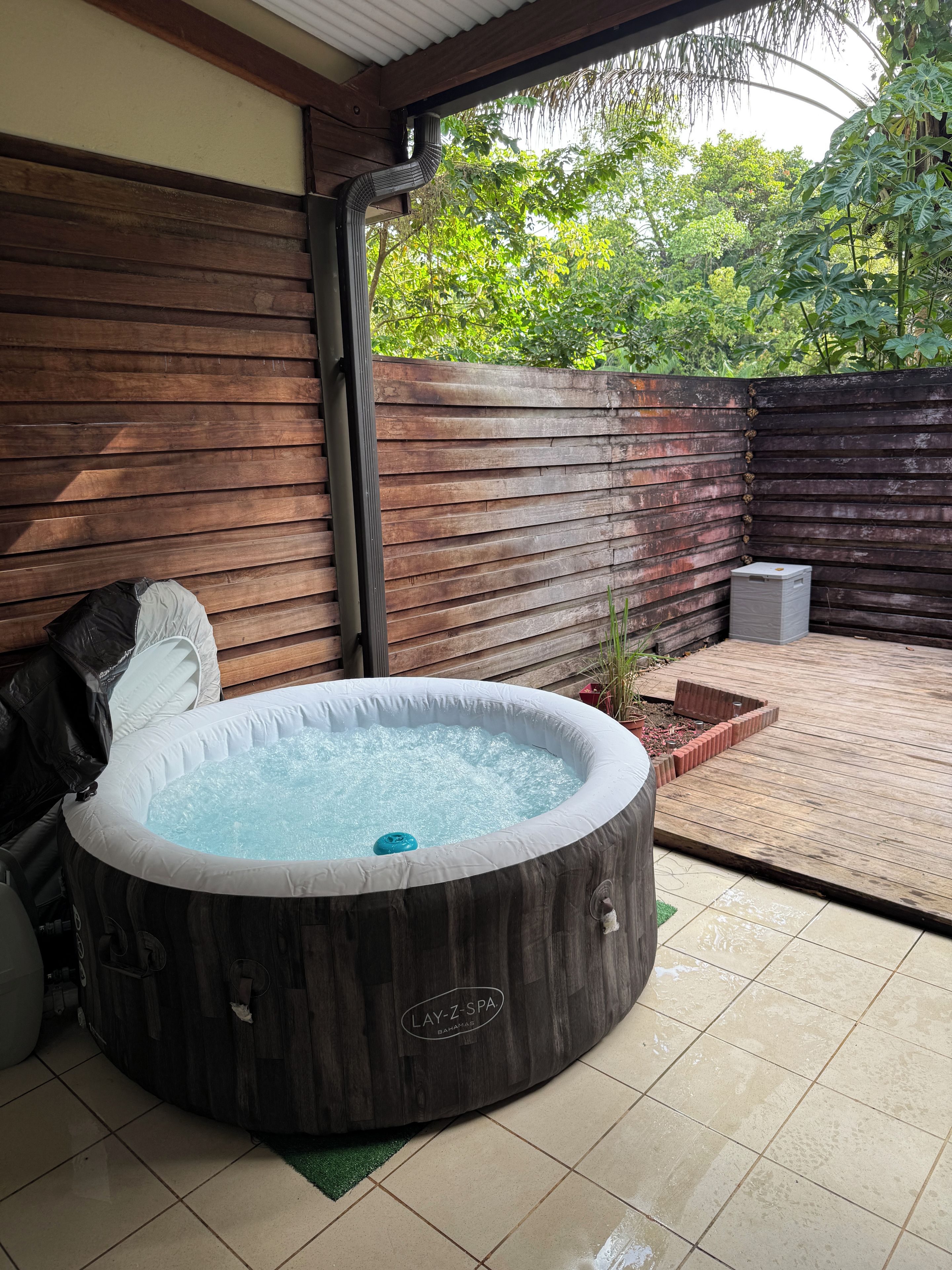 Un bain à remous avec une structure extérieure en bois, entouré d’une clôture en bois et d’une terrasse carrelée.
